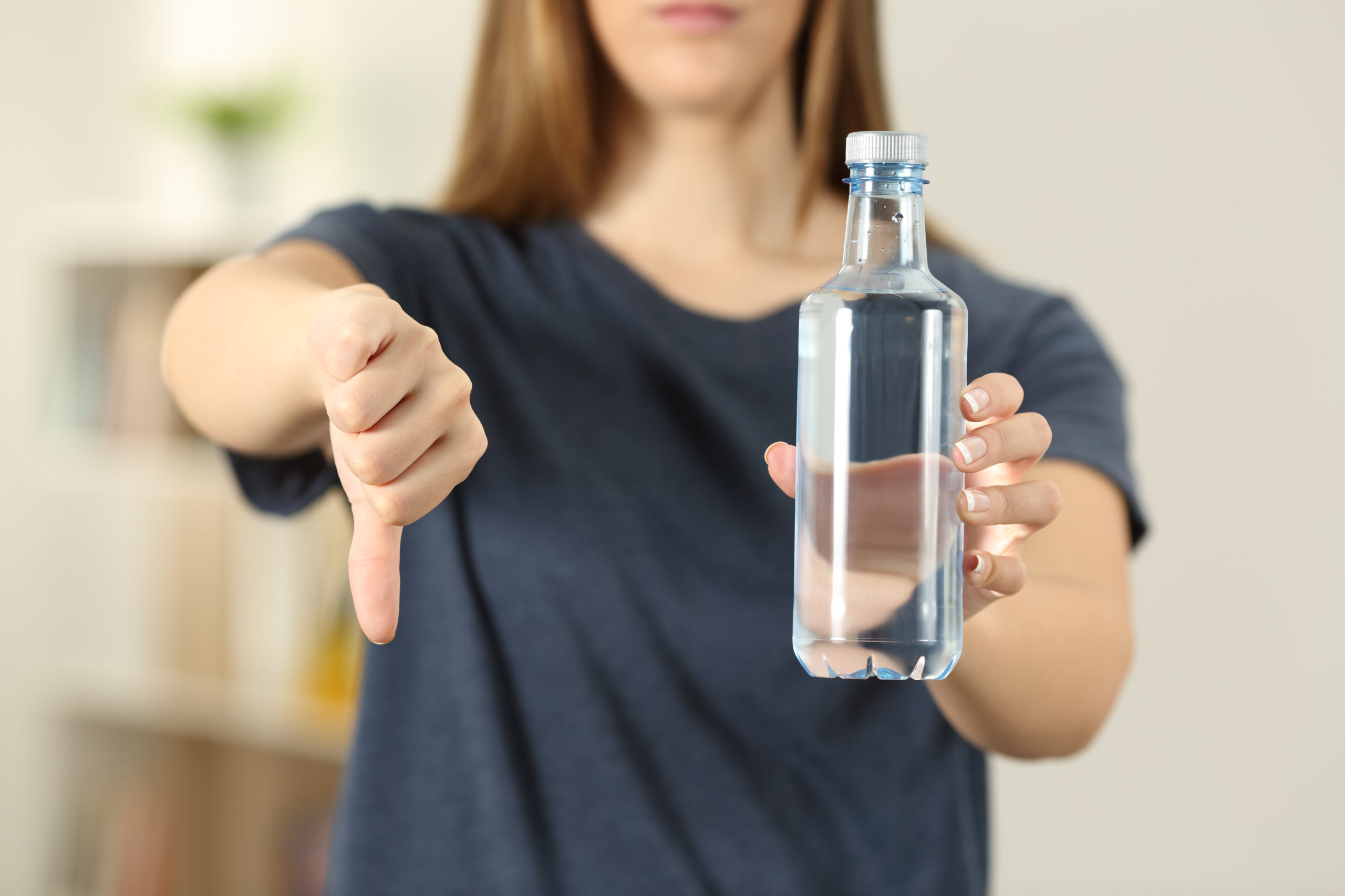 Foto einer Frau, in der einen Hand eine Plastikflasche, mit der anderen Hand Daumen nach unten